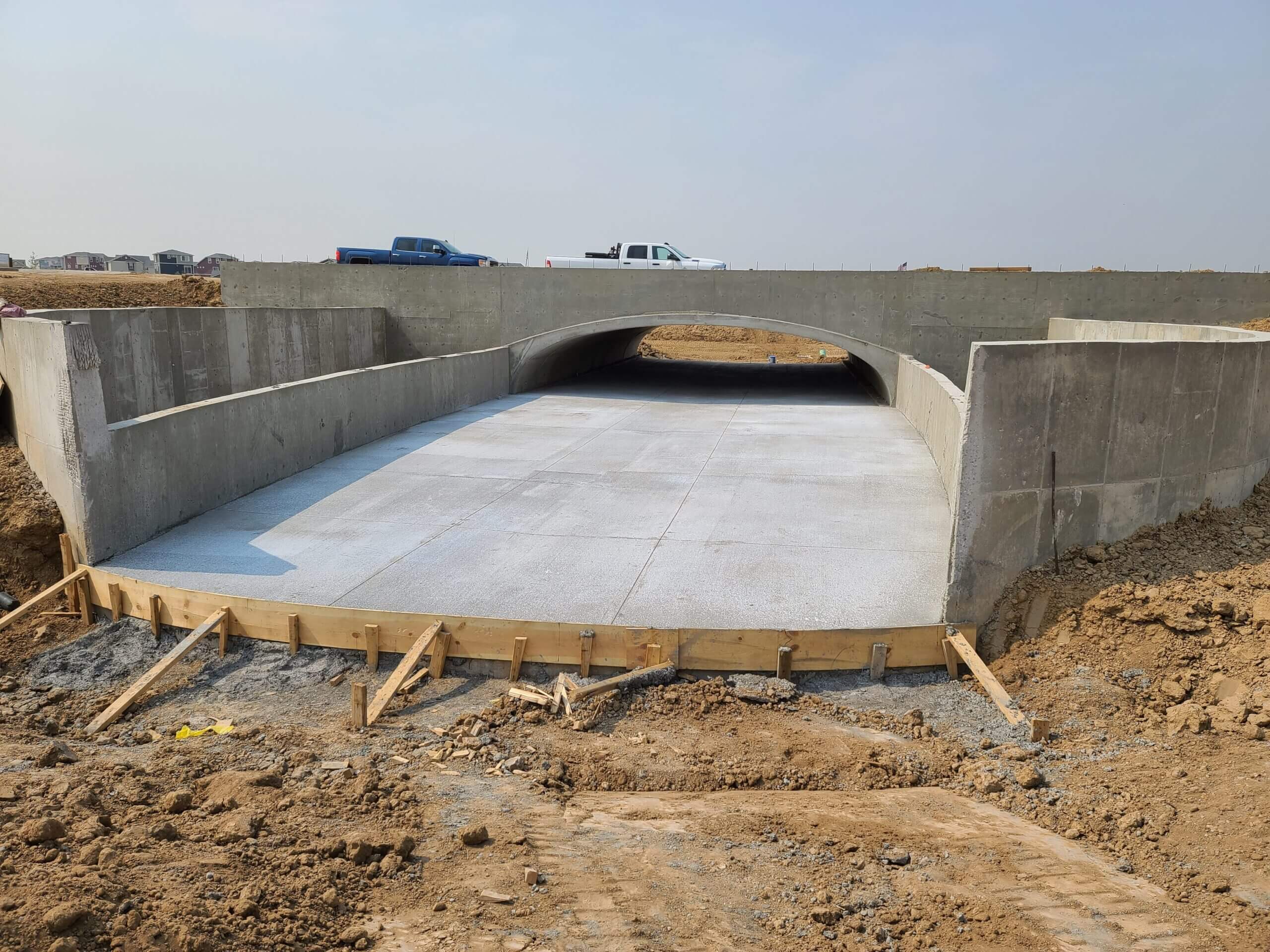 Newly constructed concrete box culvert bridge with smooth concrete channel and roadway above at a highway construction site.
