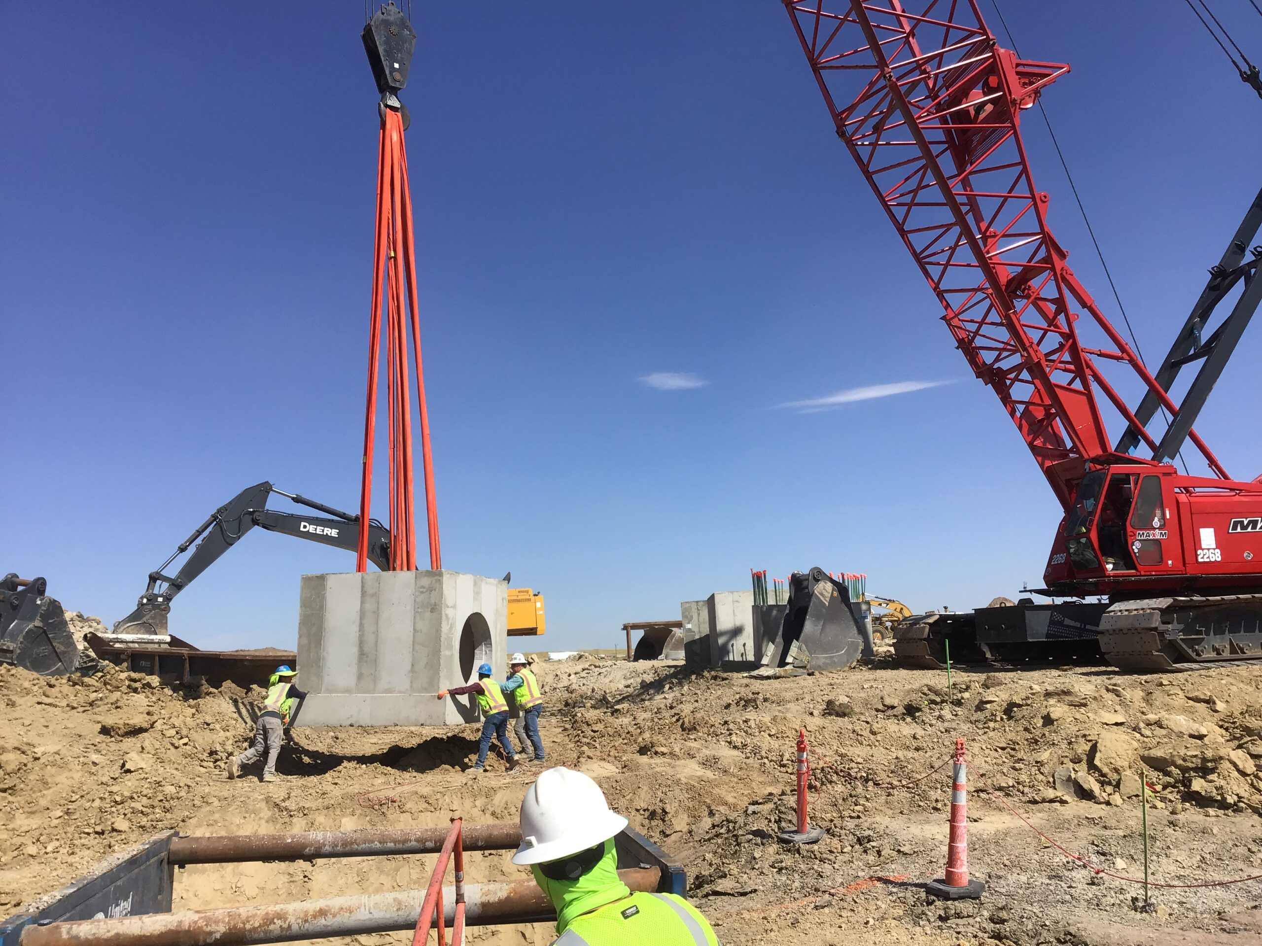 Workers guiding suspended concrete culvert section into place Workers guiding suspended concrete culvert section into place