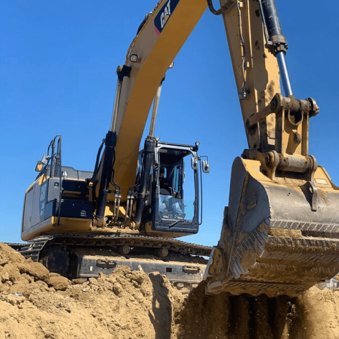 Large Caterpillar excavator digging and moving soil at an active earthmoving construction site under a clear blue sky.