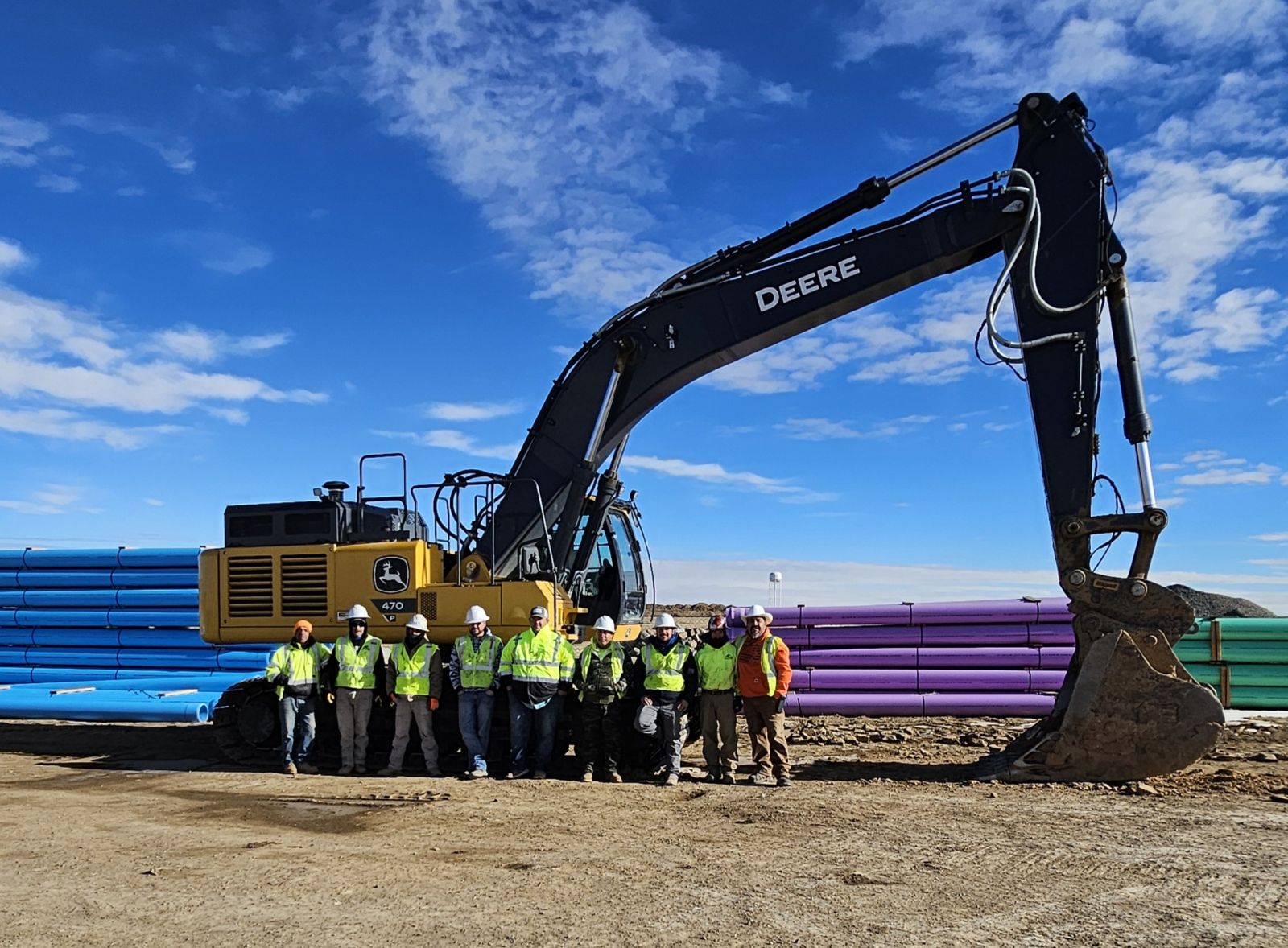 Construction crew standing in front of large excavator and stacked pipes Construction crew standing in front of large excavator and stacked pipes