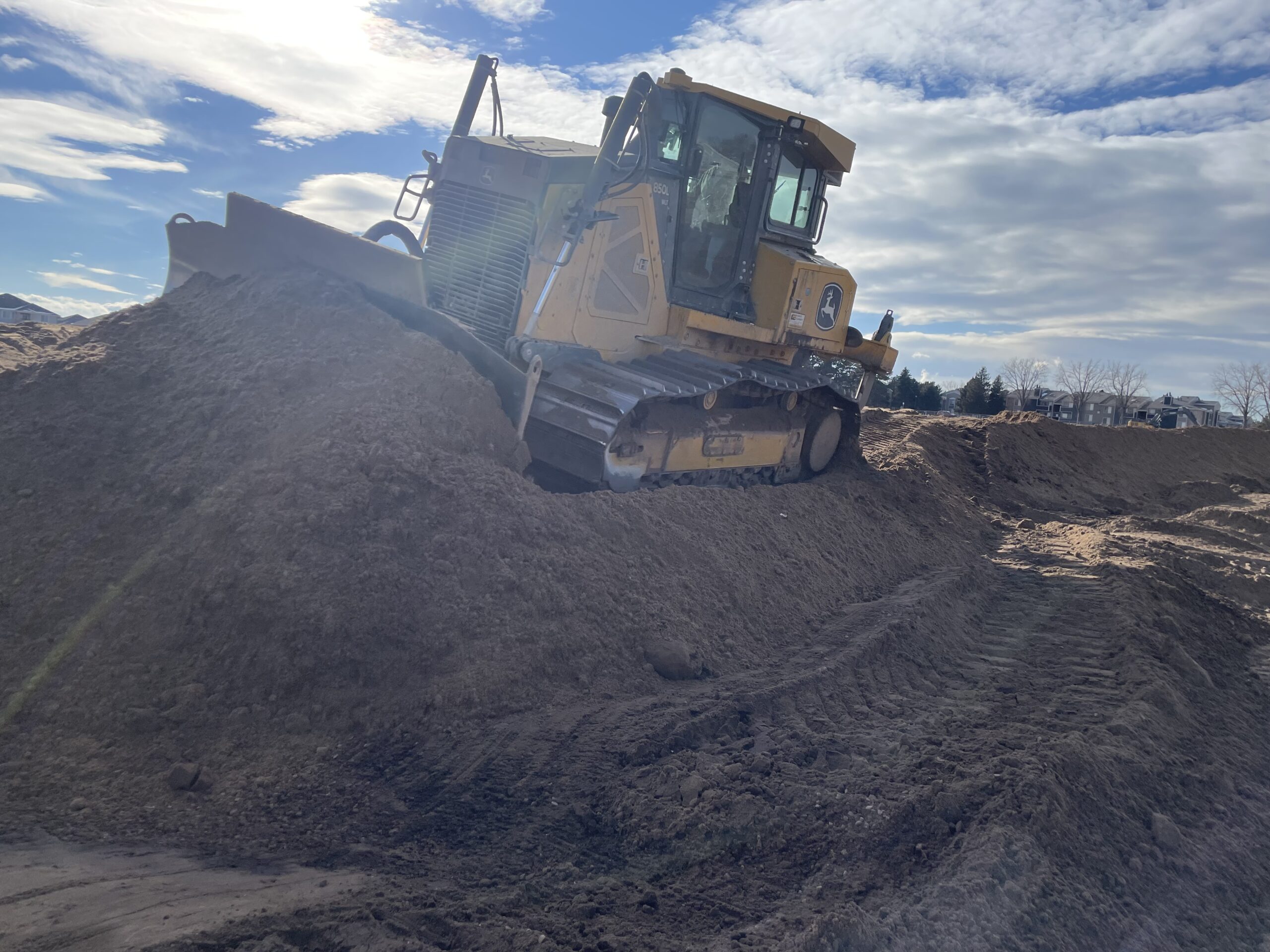 Tracked bulldozer pushing a large mound of soil during grading operations at a construction site.