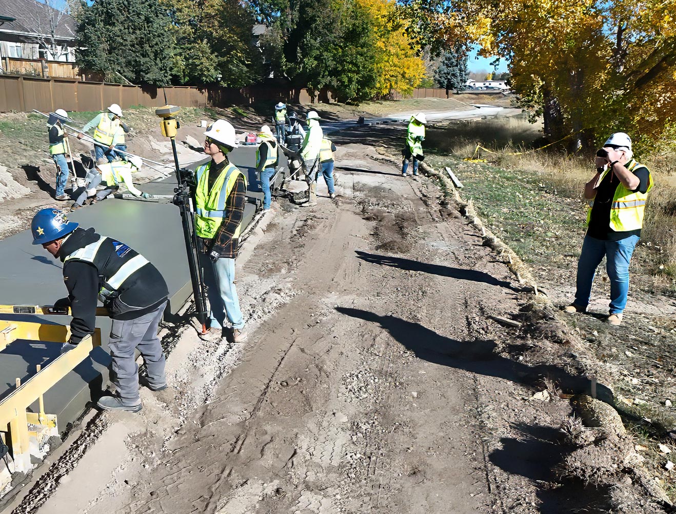 Construction crew in safety vests and hard hats pouring and finishing fresh concrete on a residential pathway using a slip form paver